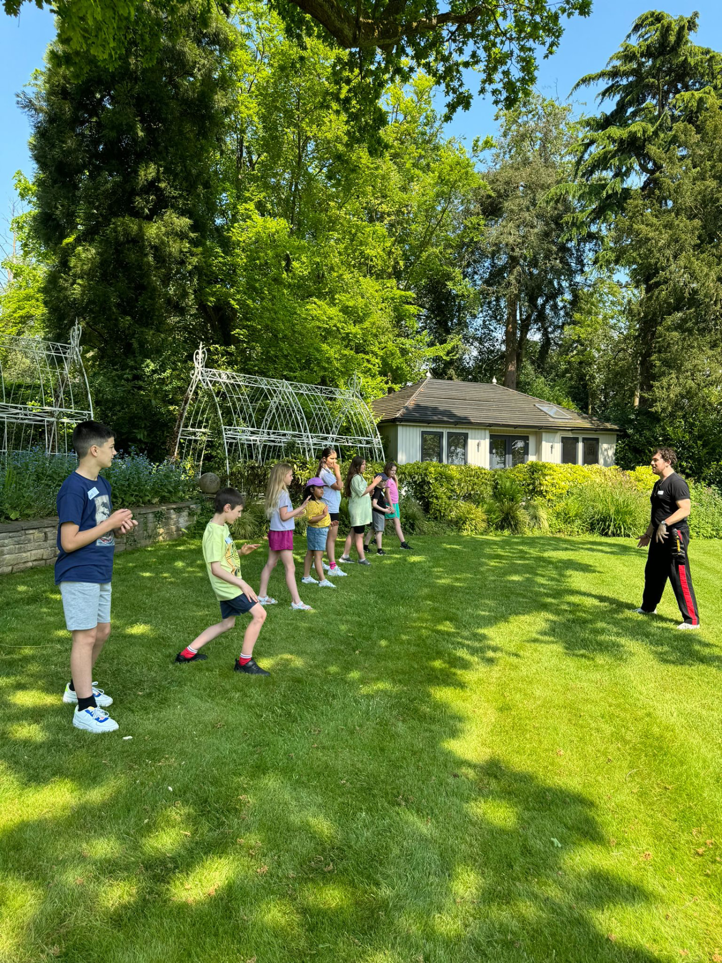 Children lined up practising martial arts stances outdoors with a coach