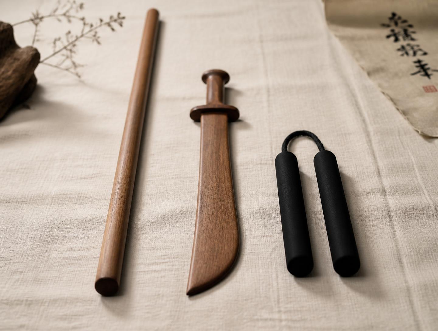 A wooden staff, wooden broadsword and foam nunchaku laid out on linen